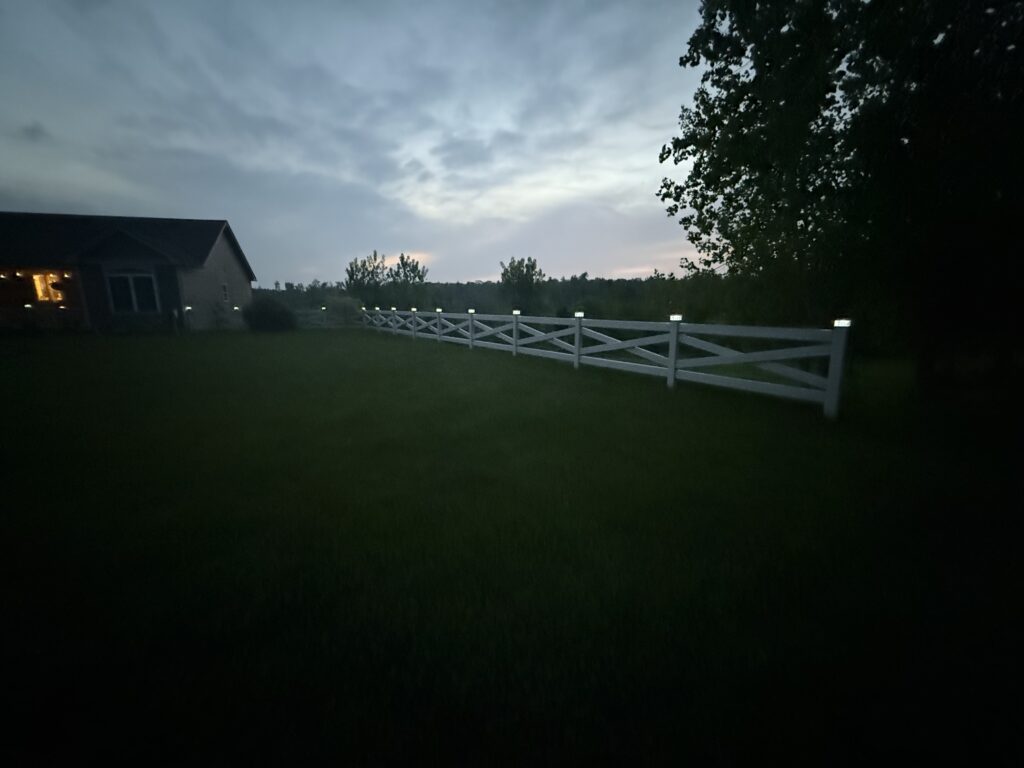 Beige vinyl crossbuck fence with solar post cap lights installed in Wilbraham MA at dusk
