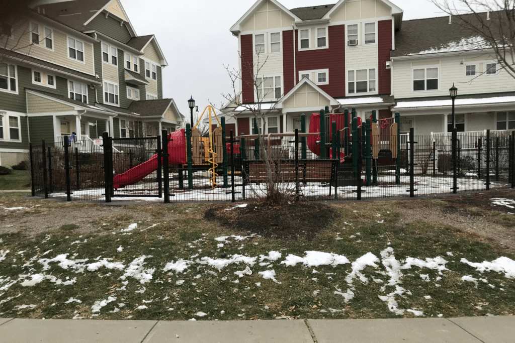 4 foot black wire fence surrounding apartment playground area in West Hartford CT with multi family buildings in background
