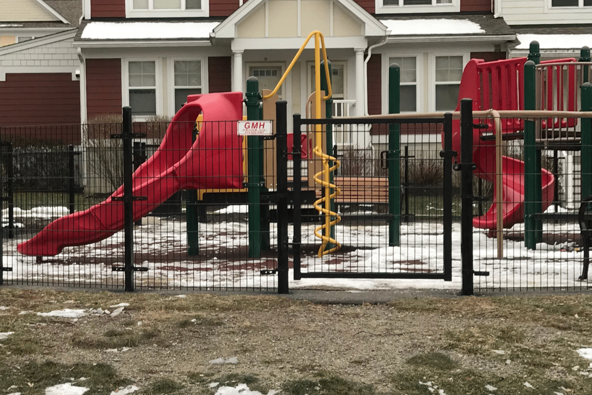 Black wire partition fence with entry gate enclosing playground at residential community in West Hartford Connecticut