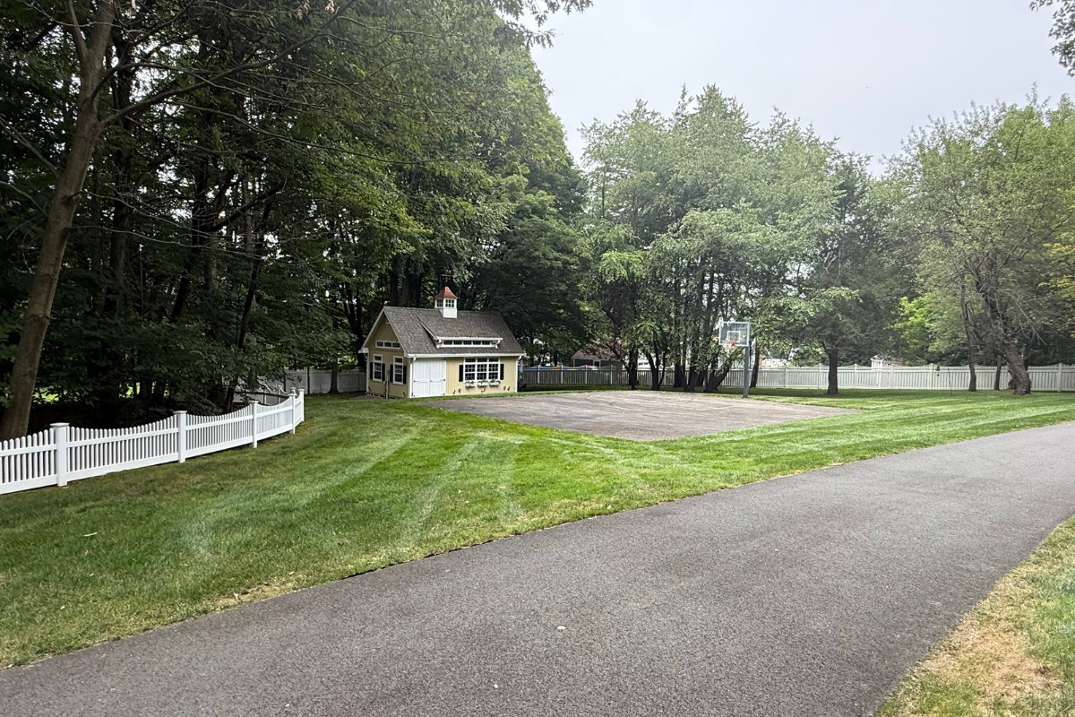 Wide view of white vinyl fence enclosing residential yard in East Longmeadow with driveway, lawn, and shed